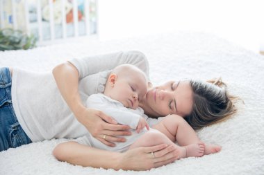 Anne ve küçük oğlu, büyük bir yatakta uyuyorlar, arkalarında yumuşak bir ışık.