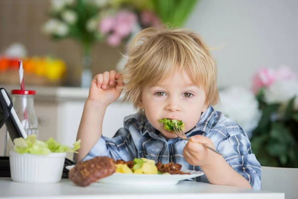 小孩子 金发男孩 在家里吃煮熟的蔬菜 花椰菜 土豆和炸鸡肉排的胡萝卜 同时看平板电影 — 图库照片