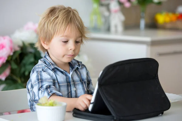 小孩子 金发男孩 一边在家里舔棒棒糖一边在平板电脑上看电影 — 图库照片