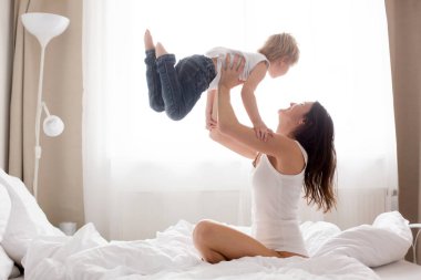 Güzel sarışın çocuk ve annesi, sabahları evde oynuyorlar, gülüyorlar, gülüyorlar ve birlikte eğleniyorlar.