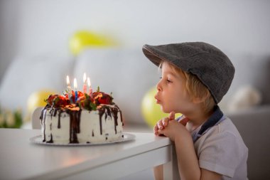 Dört yaşında sarışın bir çocuk, anaokulu çocuğu, doğum gününü evde çilekli ve çikolatalı ev yapımı pastayla kutluyor.