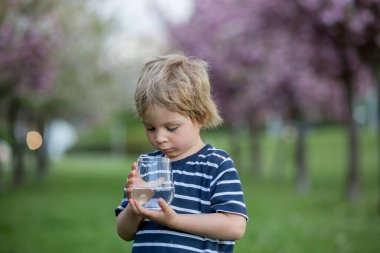 Güzel sarışın çocuk, evlat, sıcak bir yaz gününde parkta su içiyor.
