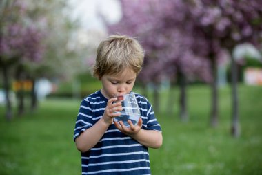 Güzel sarışın çocuk, evlat, sıcak bir yaz gününde parkta su içiyor.
