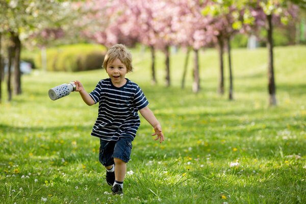 Beautiful blond child, boy, drinking water in the park on a hot summer day