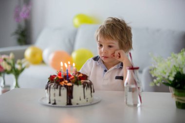 Dört yaşında sarışın bir çocuk, anaokulu çocuğu, doğum gününü evde çilekli ve çikolatalı ev yapımı pastayla kutluyor.