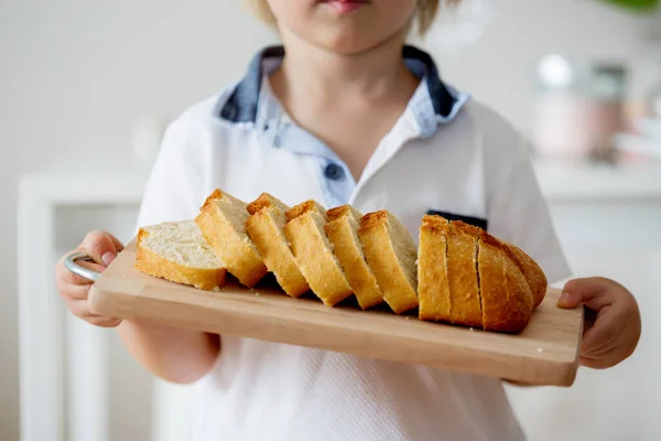 ブロンドの幼児の男の子 自家製のシアバタパンで木製のまな板を持ち 自家製焼きパンを提供しています — ストック写真