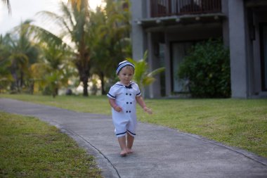 Denizci gibi giyinmiş, gün batımında kumsalda oynayan güzel bir çocuk. Ailesiyle birlikte tropik ve büyülü tatilin tadını çıkarıyor.