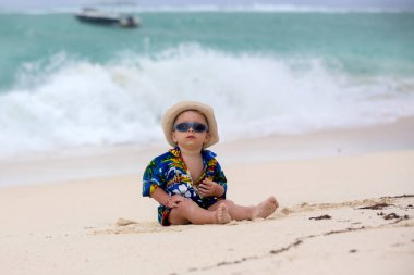 Mauritius sahilinde kumsalda oynayan, okyanus suyunun tadını çıkaran tatlı bir bebek.