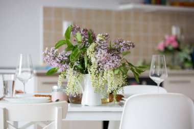 Güzel sarışın bir çocuğun yakın portresi, elinde vazoyla evde leylak taşıyan küçük bir çocuk, masada oturuyor, öğle yemeğine hazır.