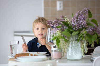 Güzel sarışın bir çocuğun yakın portresi, elinde vazoyla evde leylak taşıyan küçük bir çocuk, masada oturuyor, öğle yemeğine hazır.