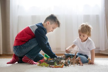 Sarışın çocuk, küçük çocuk ve ağabeyi, reşit olmamış çocuk, evde plastik oyuncaklarla oynuyorlar.
