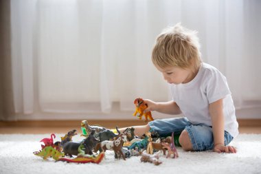 Sarışın çocuk, yeni yürümeye başlayan çocuk evde plastik oyuncaklarla oynuyor.