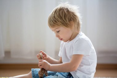 Sarışın çocuk, yeni yürümeye başlayan çocuk evde plastik oyuncaklarla oynuyor.