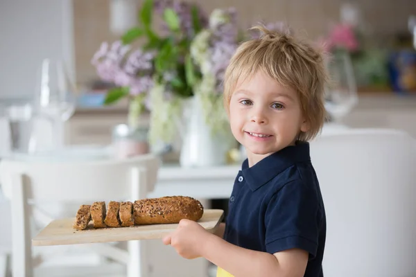 ブロンドの幼児の男の子 自家製コーンブレッドと木製のまな板を保持し 自宅で新鮮なパンを提供 — ストック写真