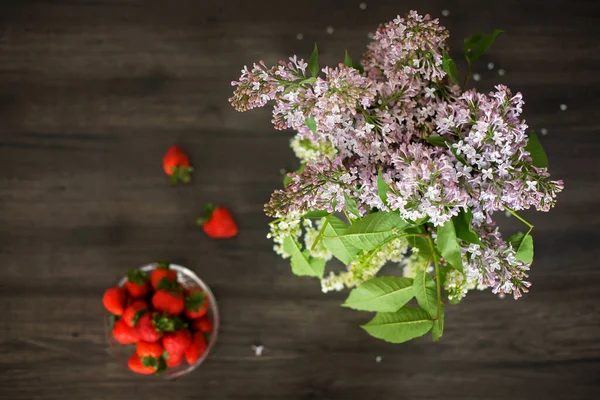 茶色の孤立した背景にライラックとイチゴ 花の花瓶と果物の入ったボウル — ストック写真