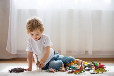 Sarışın çocuk, yeni yürümeye başlayan çocuk evde plastik oyuncaklarla oynuyor.