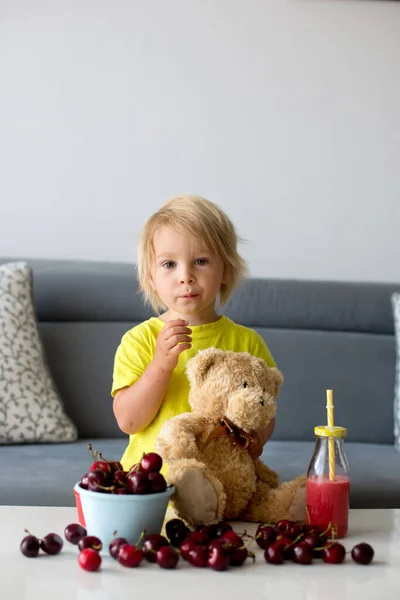 幼児ブロンド子供 かわいい男の子 食べるチェリーとともにテディベアとともに自宅 — ストック写真