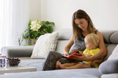 Sevimli anne, evde vişne yiyen küçük bebeğine bir kitapta resimler gösteriyor.