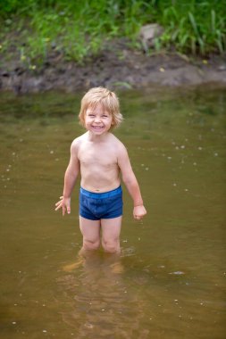 Şirin çocuk, evlat, gölde yüzüyor, kameraya gülümsüyor.