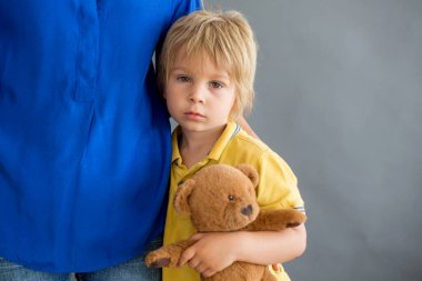 Üzgün küçük çocuk, sarışın çocuk, evde annesine sarılıyor.