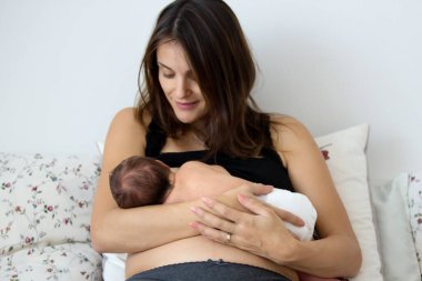 Genç anne bebeğini emziriyor, onu kollarına alıyor ve mutluluktan gülümsüyor.