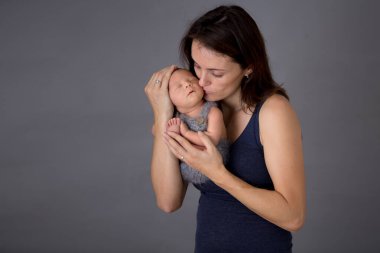 Anne, yeni doğan oğlunu gri arka planda öpüyor ve kucaklıyor. Şefkatli, özenli, sevgi dolu. Kadın ve küçük bebek portresi, mutluluk konsepti, izole edilmiş görüntü.