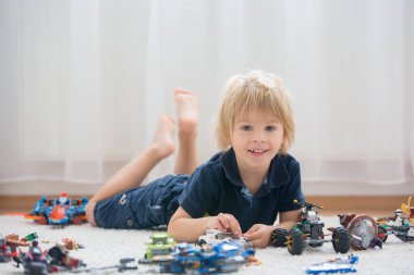 Tatlı çocuk, sarışın çocuk, Colofrul plastik bloklarla oynuyor, inşaat oyuncakları, araba ve uçak yapıyor.