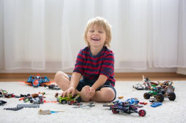 Tatlı çocuk, sarışın çocuk, Colofrul plastik bloklarla oynuyor, inşaat oyuncakları, araba ve uçak yapıyor.