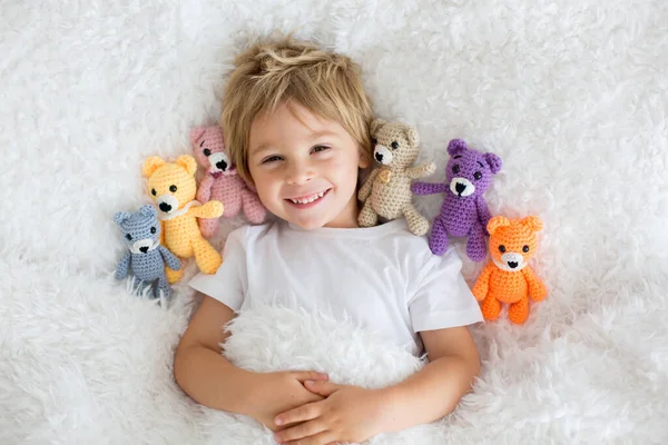 小さな幼児の子供 かわいいブロンドの男の子 多くのテディベアとベッドに横たわっ 手作りAmigurumiおもちゃ — ストック写真