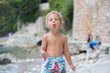 Cute child, blond toddler boy, holding sea urchin on the beach, summertime clipart