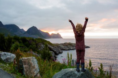 Şirin bir çocuk, Kuzey Norveç, Senja Adası 'ndaki Husoy kayasından inanılmaz bir manzaranın keyfini çıkarıyor. Norveç 'in İskandinav topraklarında inanılmaz güzel manzara ve görkemli doğa