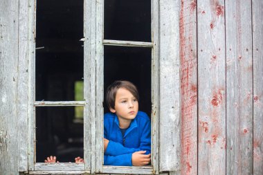Üzgün çocuk, Norveç 'teki harap olmuş eski binanın penceresinden dışarı bakıyor.