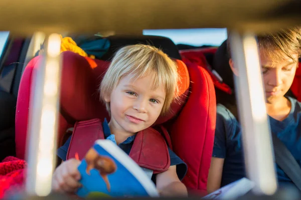 男の子の兄弟 車で休暇に旅行し 車の座席に座って本を読んだり モバイルで遊んでいます — ストック写真