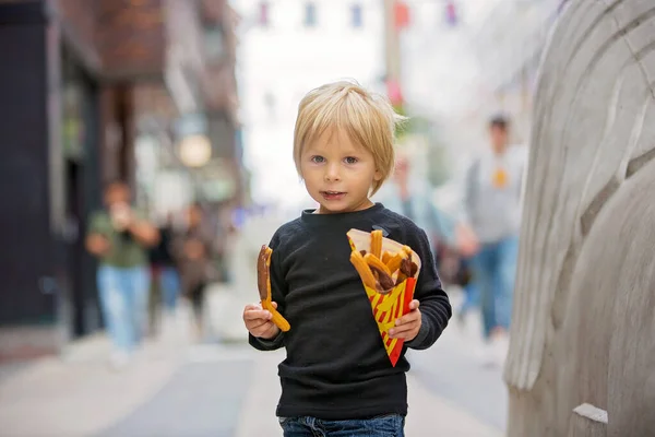 Cute blond child with black shirt, eating churros on the street in the city of Stockhlom, sweet desert sold on every corner of the city, Sweden. Traditional Spanish and Portuguese cuisine desert