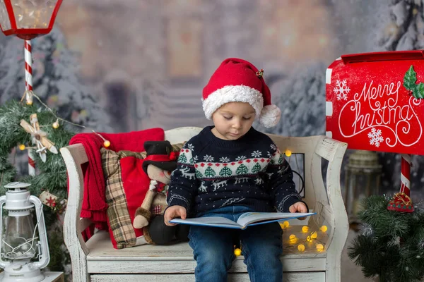 美しい子供 金髪の幼児の少年 本を読んで 彼の周りのクリスマスの装飾が施されたベンチに座って — ストック写真