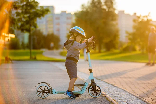 かわいい就学前の子供 日没のスクーターで公園で遊ぶ — ストック写真