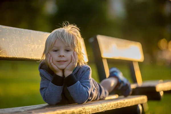 一个可爱的金发碧眼的孩子的近照 小伙子 夏天的时候 他躺在公园的长椅上 — 图库照片