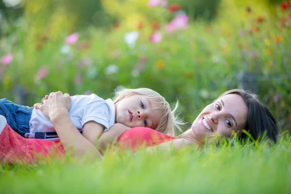 妈妈和可爱的金发碧眼的孩子 躺在草地上 互相拥抱 彼此享受着片刻的柔情 — 图库照片