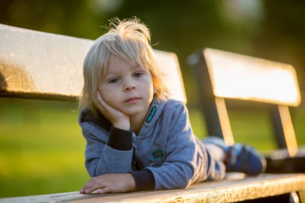 一个可爱的金发碧眼的孩子的近照 小伙子 夏天的时候 他躺在公园的长椅上 — 图库照片