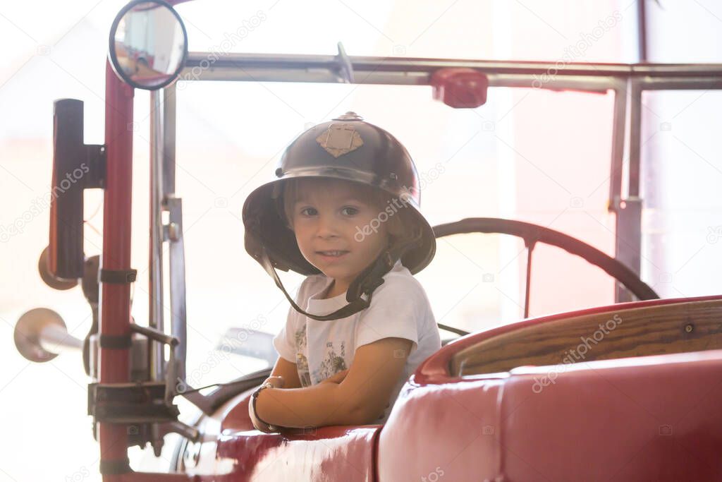 Child, cute boy, dressed in fire fighers cloths in a fire station with fire truck, childs dream