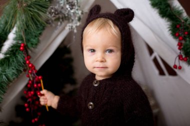 Sevimli bebek bebek çocuk teepee içinde oynarken el yapımı örgü ayı kostümlü Noel, kahverengi zemin üzerinde atış stüdyo dekore edilmiş