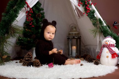 Sevimli bebek bebek çocuk teepee içinde oynarken el yapımı örgü ayı kostümlü Noel, kahverengi zemin üzerinde atış stüdyo dekore edilmiş