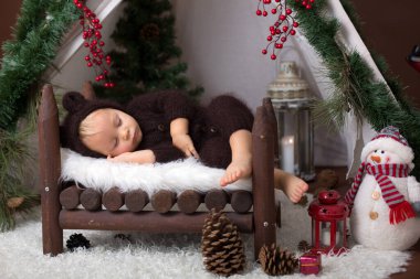 Ahşap teepee yatakta uyuyan sevimli bebek bebek çocuk el yapımı örgü ayı kostümlü, Noel için dekore edilmiştir.