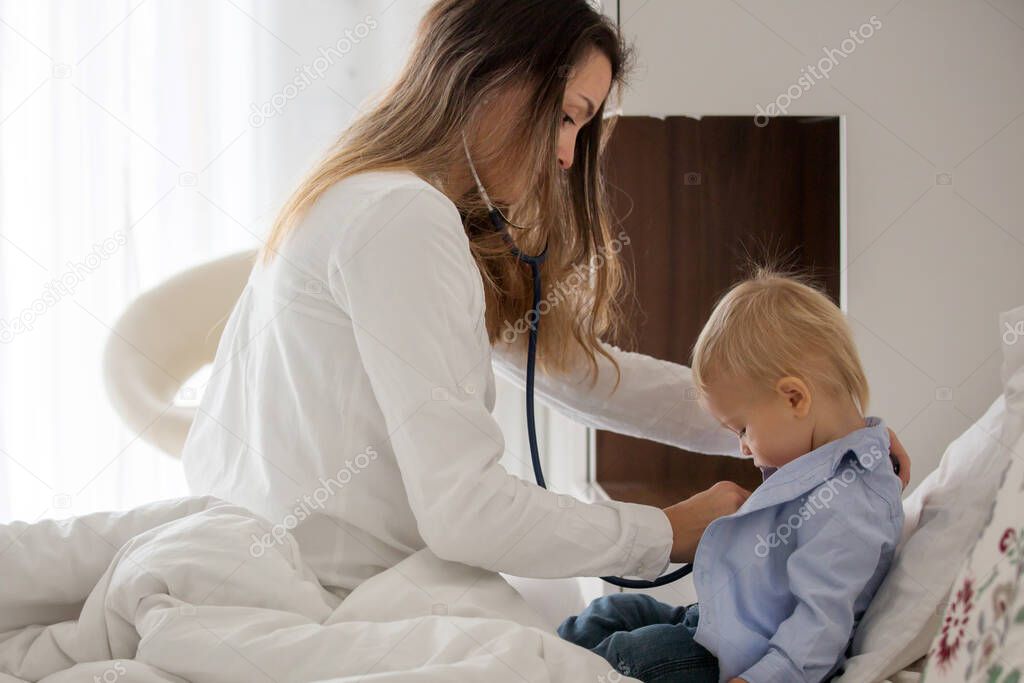 Young doctor, examiing sick baby boy on a home visitation, child lying ill in bed