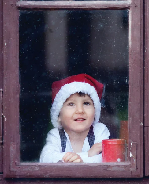 Roztomilý chlapec, dívá se oknem, čeká na Santu — Stock fotografie