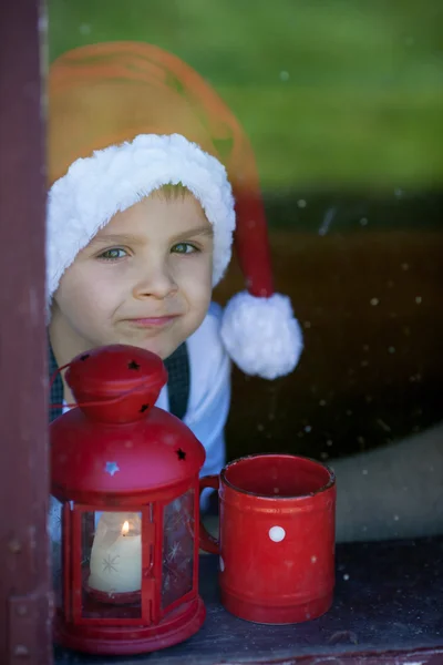 Liebenswerter Junge, der aus dem Fenster schaut und auf den Weihnachtsmann wartet — Stockfoto