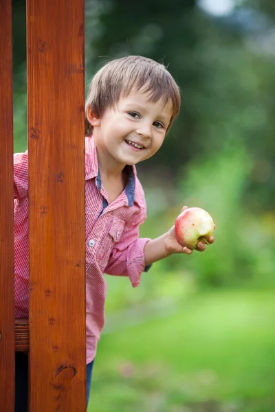 Adorable boy, holding apple, standing next to a door — Stock Photo, Image