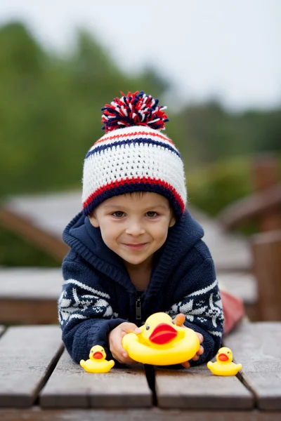 Entzückender kleiner Junge, der draußen auf einem Ast mit Gummienten spielt — Stockfoto