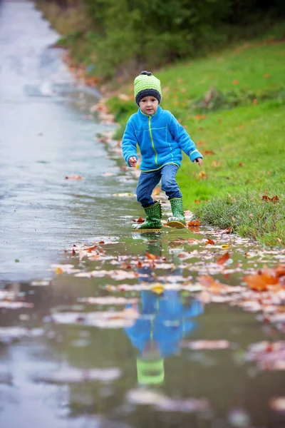 小さな男の子が、泥だらけの水たまりにジャンプ — ストック写真