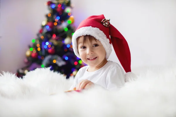 Lindo chico adorable leyendo un libro delante del árbol de Navidad —  Fotos de Stock